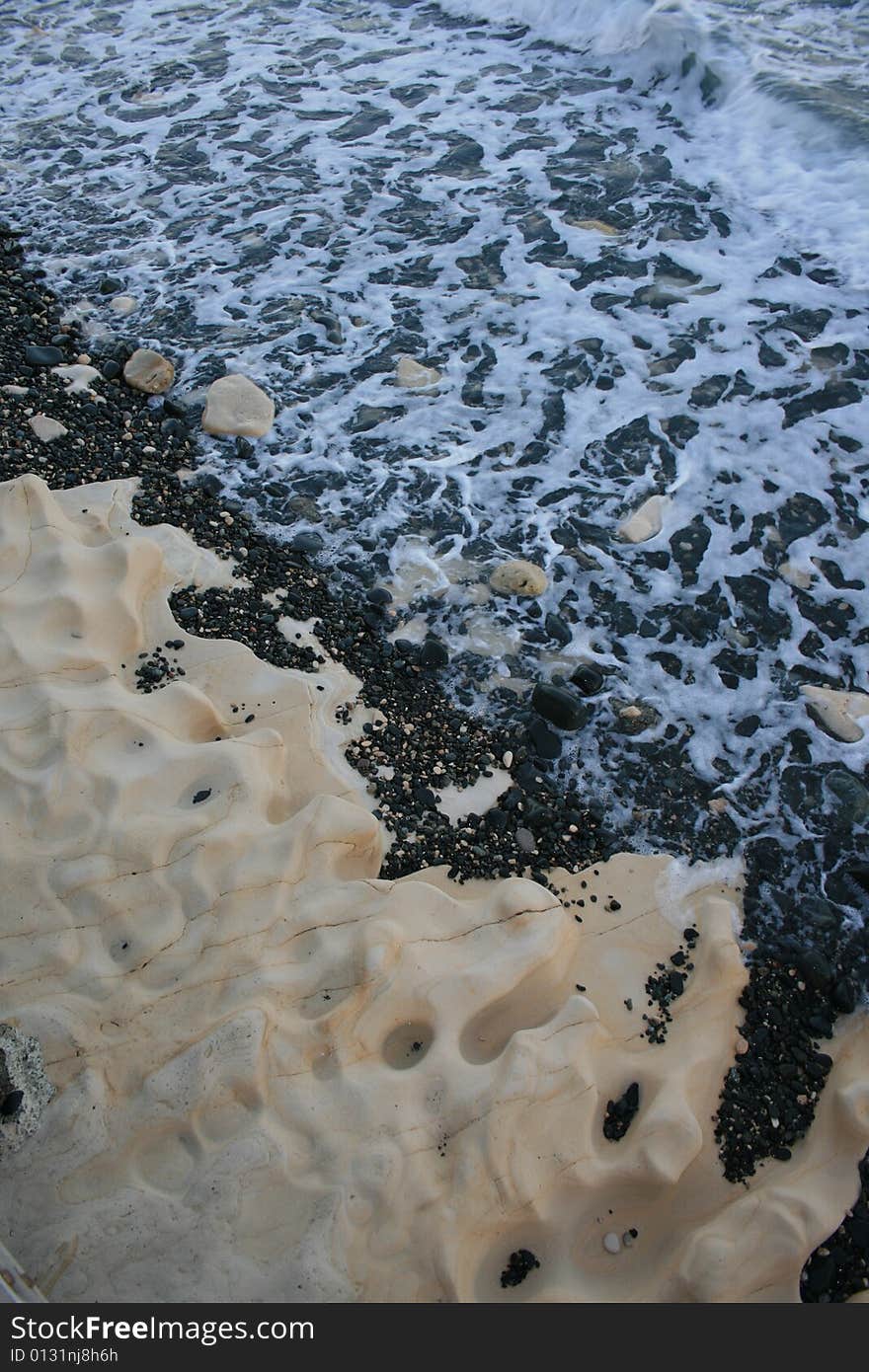 A closeup of foamy waves breaking on the sandstone shore covered with black pebbles. A closeup of foamy waves breaking on the sandstone shore covered with black pebbles