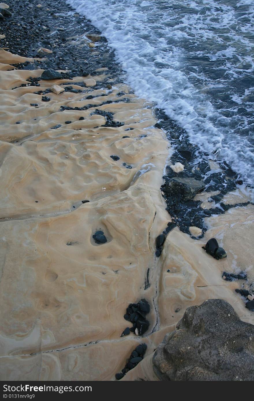 A closeup of foamy waves breaking on the sandstone shore covered with black pebbles. A closeup of foamy waves breaking on the sandstone shore covered with black pebbles