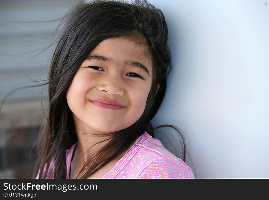 Happy six year old girl standing against wall outdoors