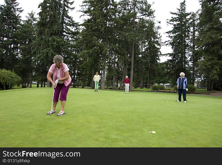 Elderly woman teeing off on the golf course as her three friends watch. Horizontally framed photo.