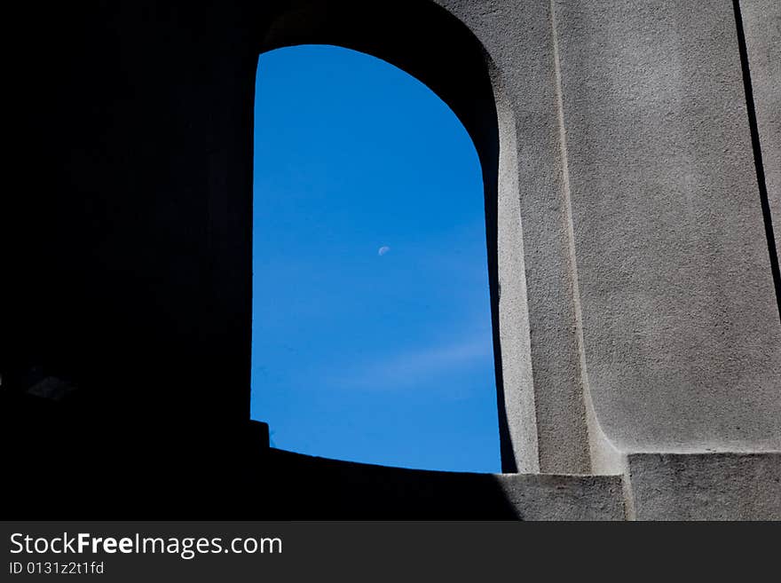 Stone arch, half in the shadow half in sunlight with blue sky and a day moon visible thru the opening. Stone arch, half in the shadow half in sunlight with blue sky and a day moon visible thru the opening.