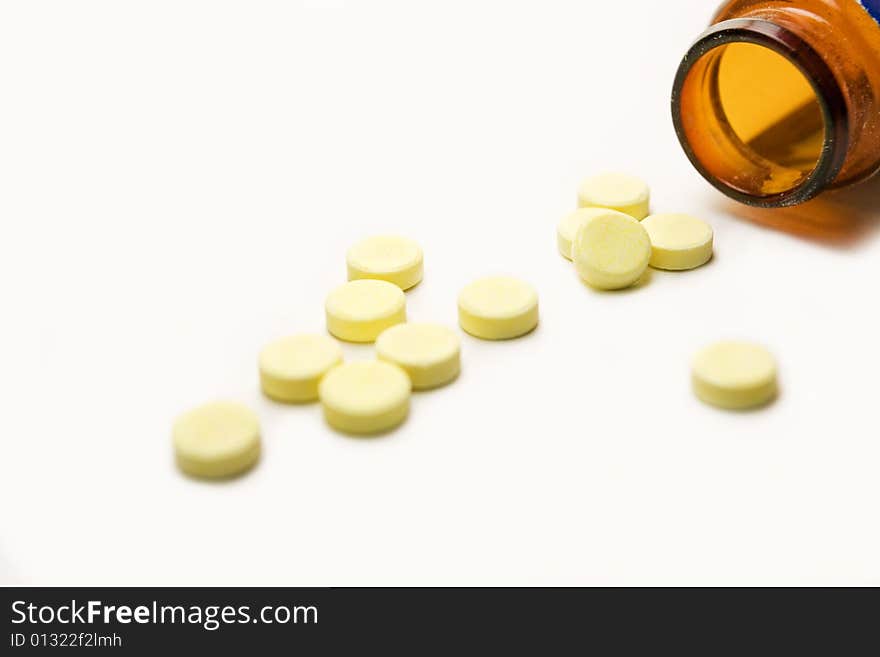 A few yellow pills and container, isolated over white background