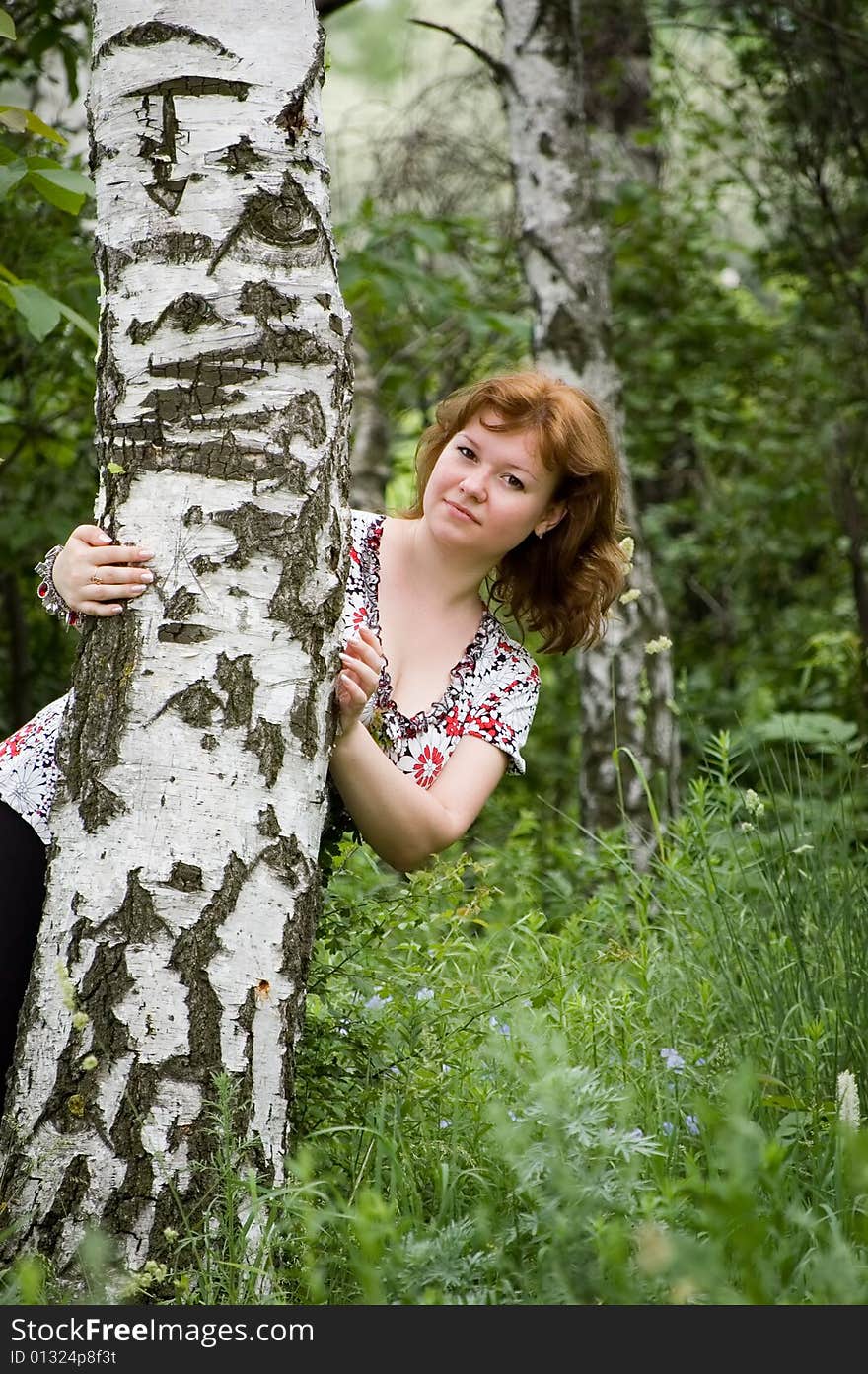 The brown-haired woman keeps for a birch and looks out from it. The brown-haired woman keeps for a birch and looks out from it