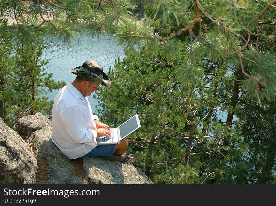 Man working on a laptop on the rocks. With copy space - you can place what you wish on the monitor. Man working on a laptop on the rocks. With copy space - you can place what you wish on the monitor.