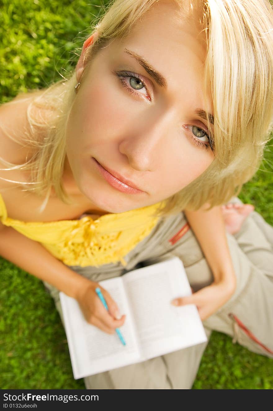 Sad young girl sitting oudoors on a grass and reading book