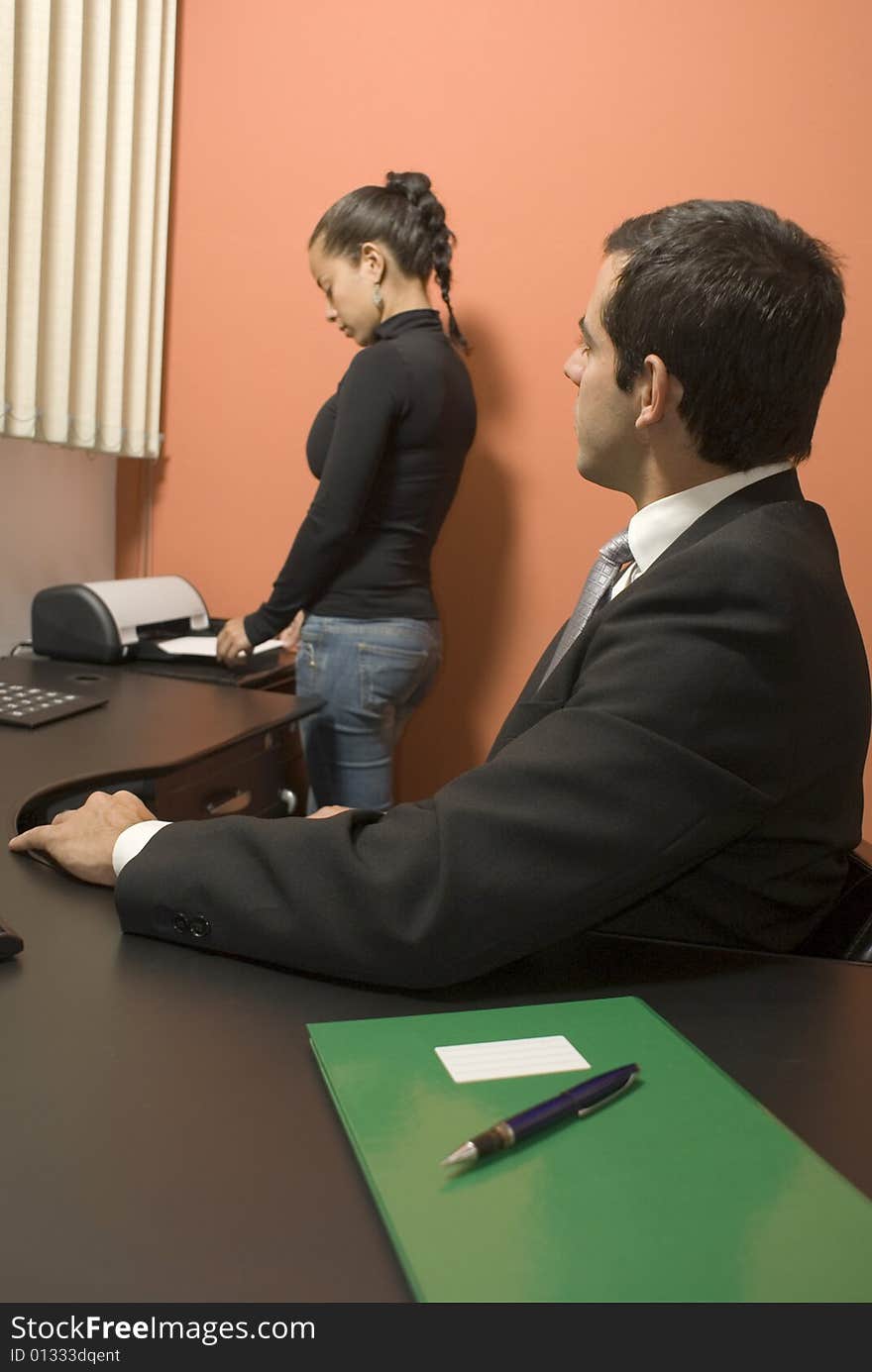 Businessman watches his secretary use the fax machine while sitting at his desk. Vertically framed photo. Businessman watches his secretary use the fax machine while sitting at his desk. Vertically framed photo.