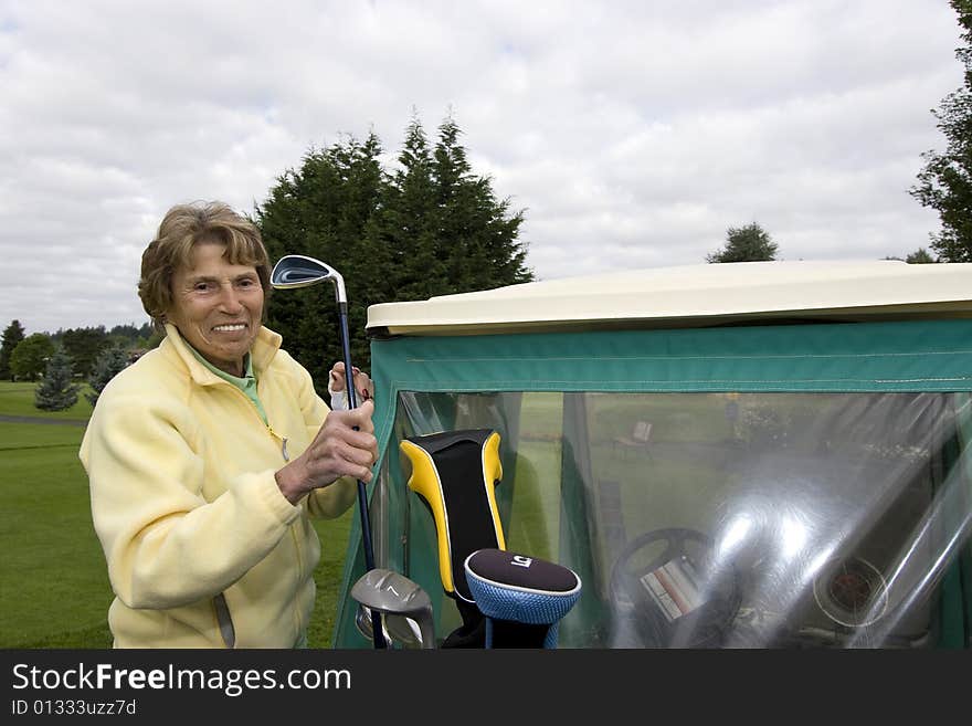 Female elderly woman puts golf club in golf cart. Horizontally framed photo. Female elderly woman puts golf club in golf cart. Horizontally framed photo.