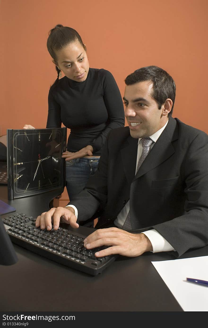 Office woman shows a businessman a giant clock while he types on his computer. Vertically framed photo. Office woman shows a businessman a giant clock while he types on his computer. Vertically framed photo.