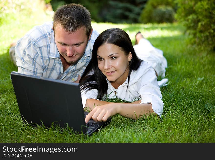 Couple lying on grass with laptop. Couple lying on grass with laptop