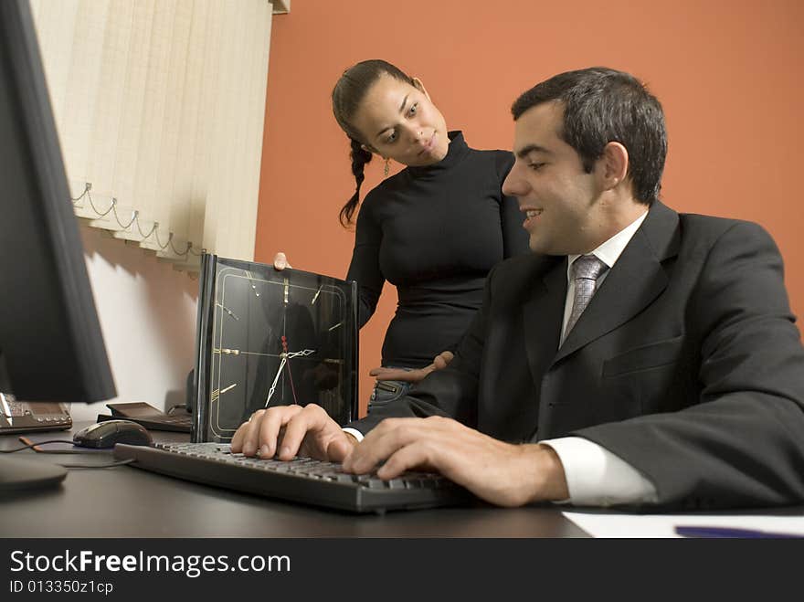 Office woman shows a businessman a giant clock while he types on his computer. Horizontally framed photo. Office woman shows a businessman a giant clock while he types on his computer. Horizontally framed photo.