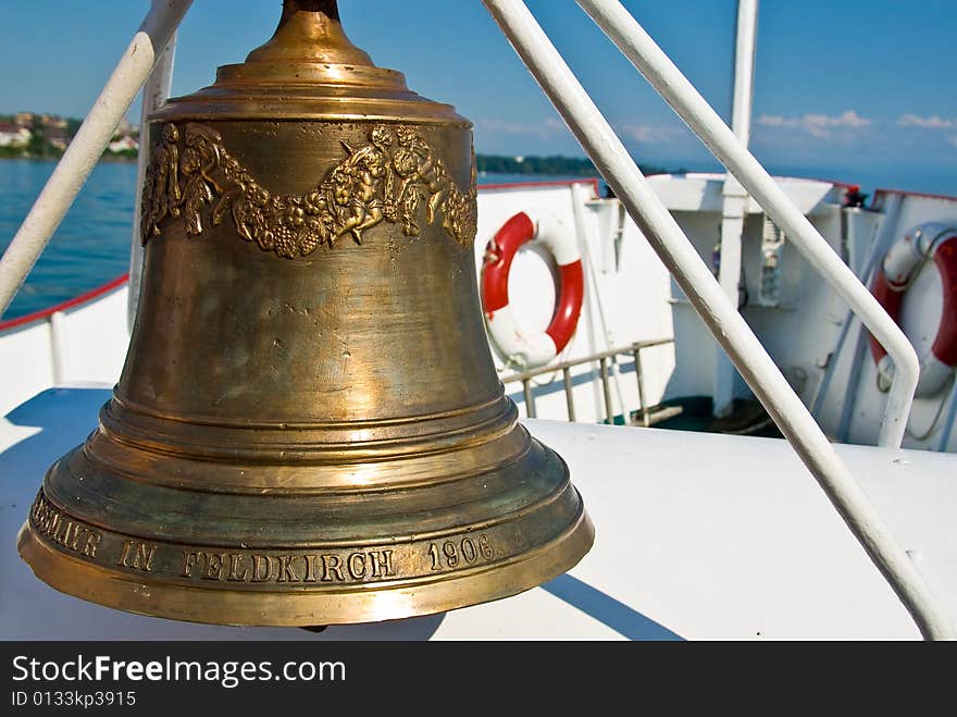 A golden ship's bell with the lake of constance in the background. A golden ship's bell with the lake of constance in the background