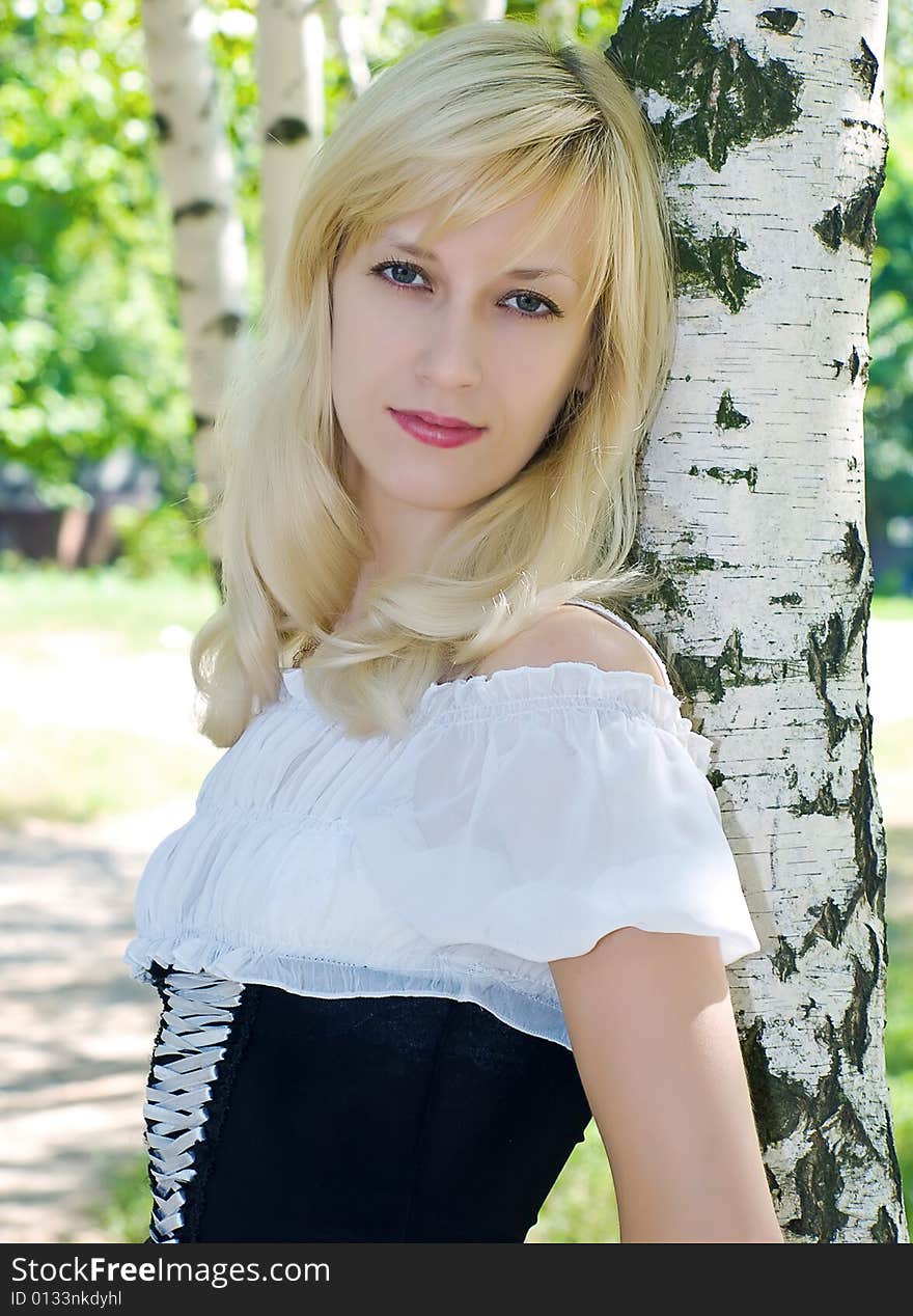 Portrait of pretty blonde girl near of birch stem