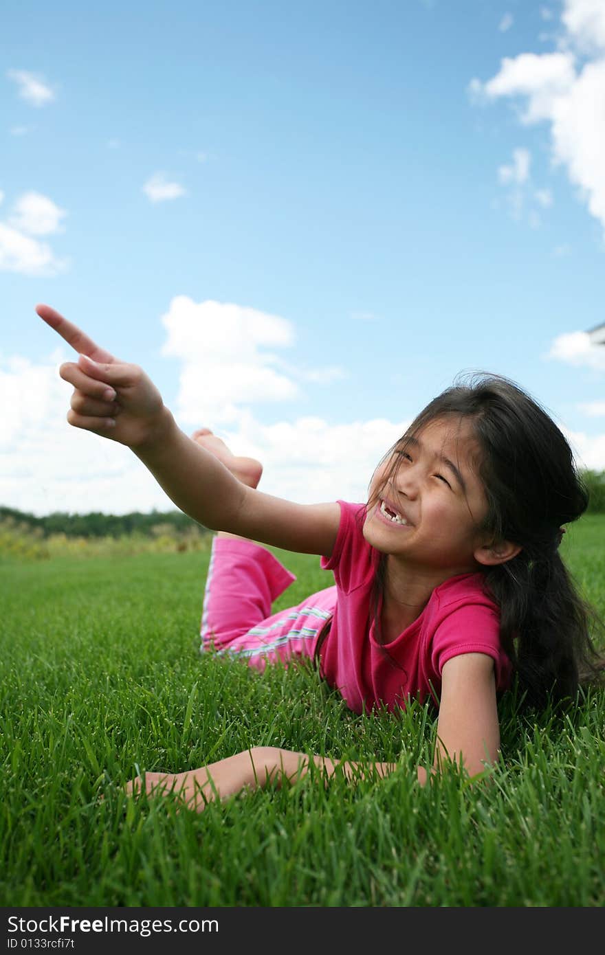 Little girl lying on grass in summer pointing up