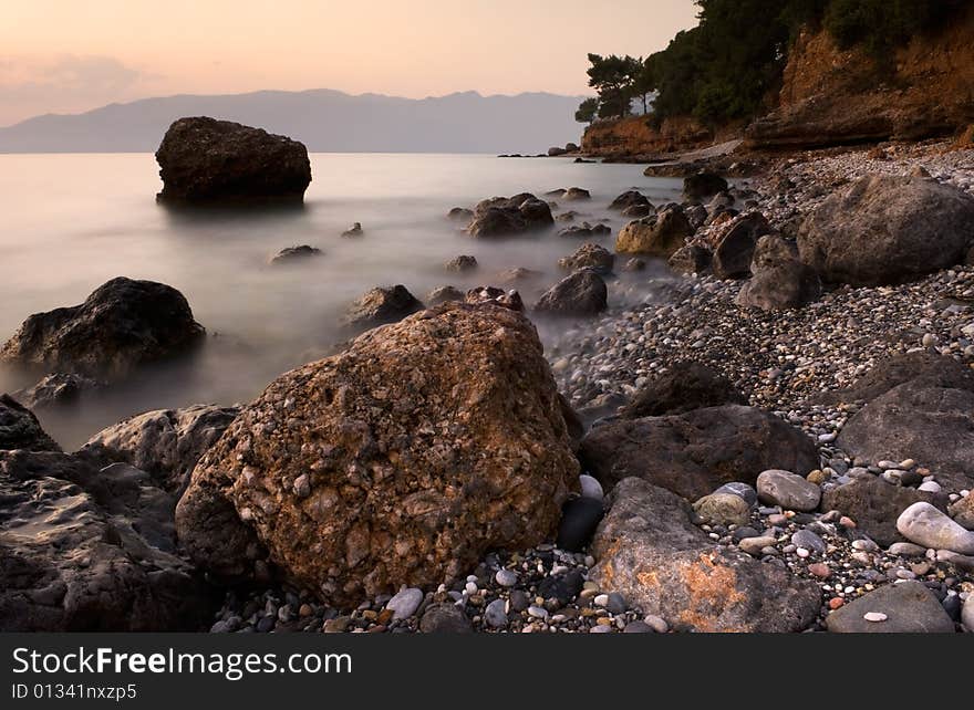 Image shows a rocky mediterranean seascape, photographed with a long exposure right after sunset.