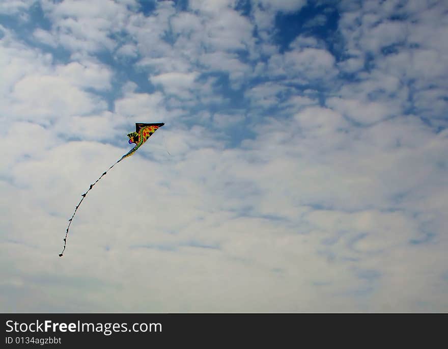 A colorful kite flying high in a blue sky of puffy white clouds. A colorful kite flying high in a blue sky of puffy white clouds