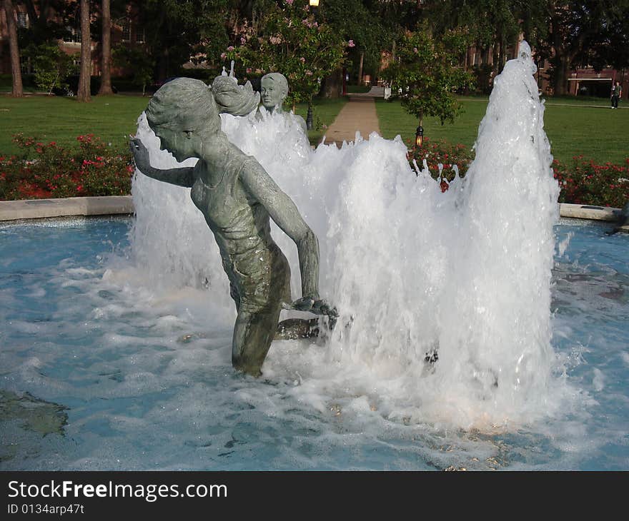 This is a water fountain that has bronze statues of people playing and having fun. This is a picture perfect college day. This is a water fountain that has bronze statues of people playing and having fun. This is a picture perfect college day.