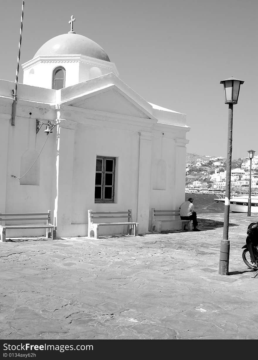 A black and white image of a man backed to a Greek church in Mykonos, Greece. A black and white image of a man backed to a Greek church in Mykonos, Greece.