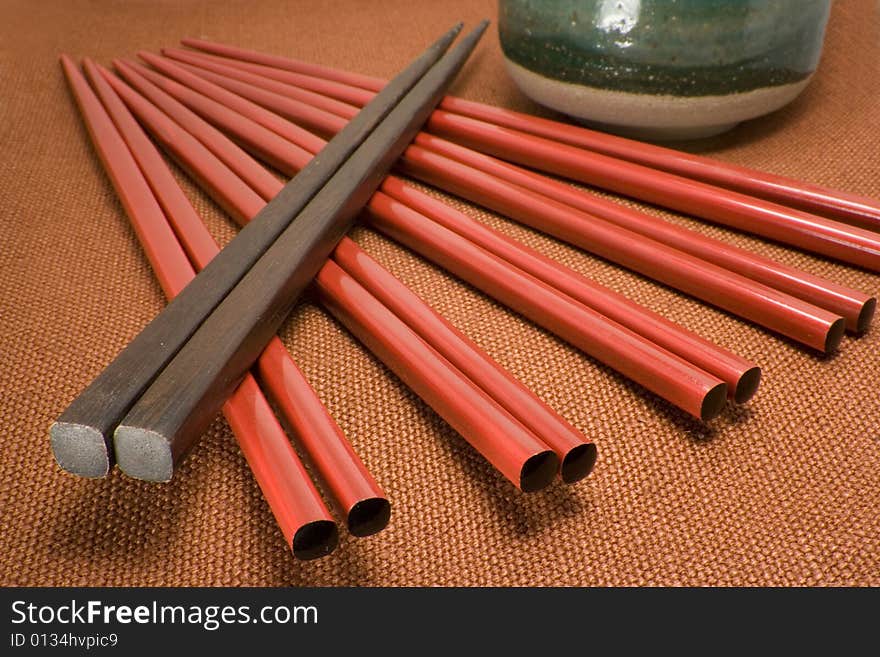 Red and brown chopsticks arranged diagonally leading to tea cup