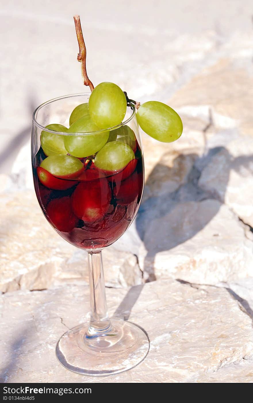 Red wine glass with grapes cluster over stone background. Red wine glass with grapes cluster over stone background