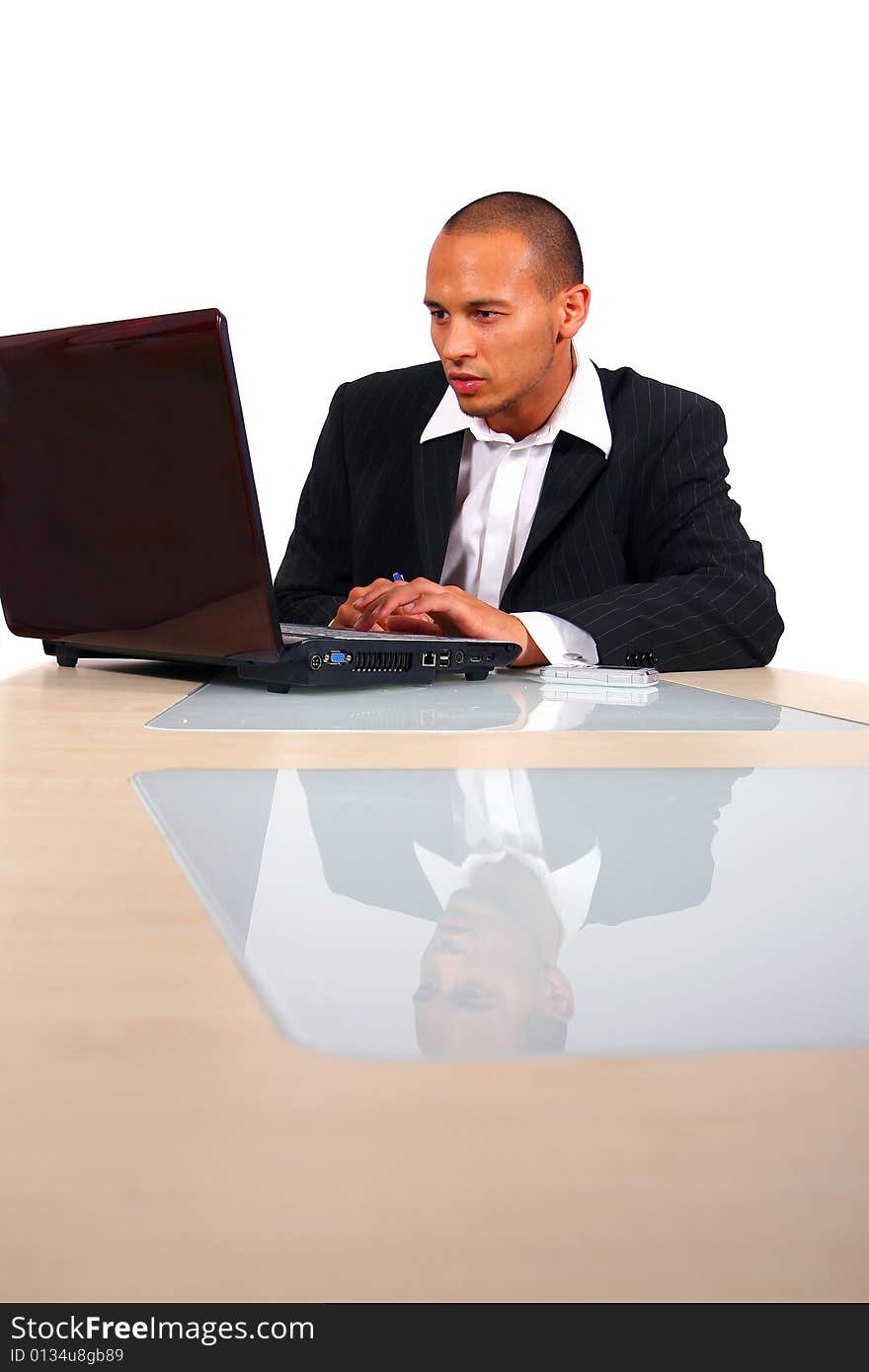 A young businessman sitting by desk at office working on the laptop with cellphone on the table. Isolated over white. A young businessman sitting by desk at office working on the laptop with cellphone on the table. Isolated over white.