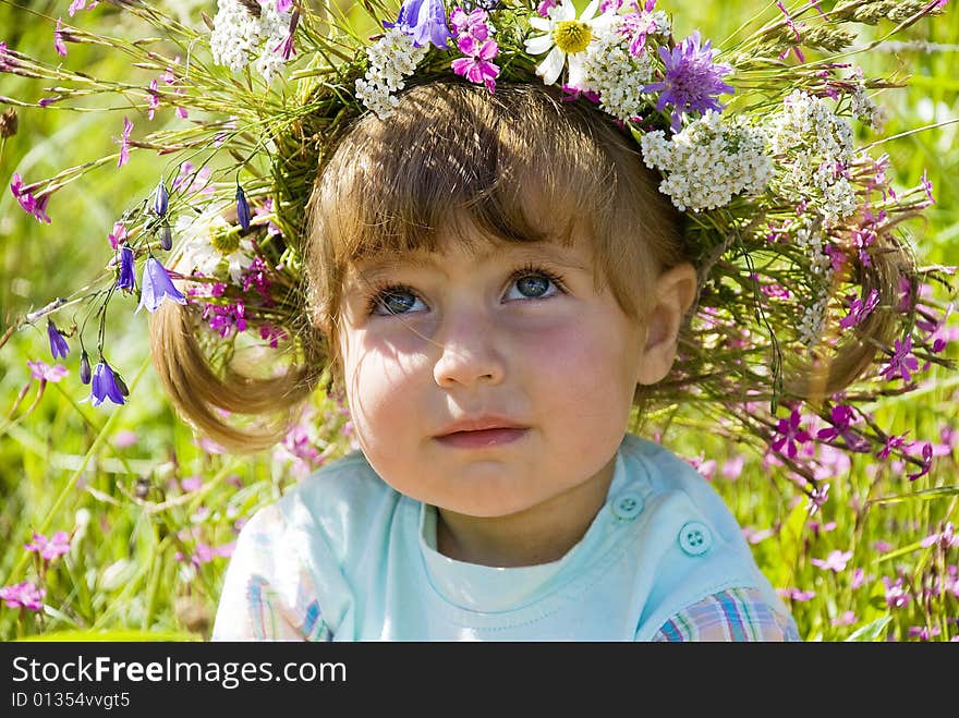 The little girl in wildflower diadem thoughtfully looks in the sky. The little girl in wildflower diadem thoughtfully looks in the sky.