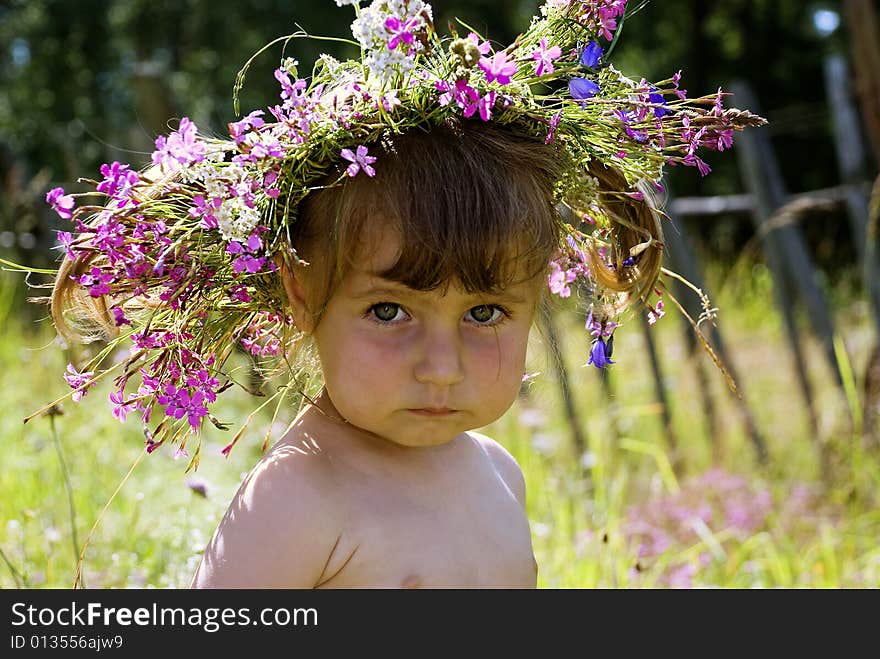 The little girl in wildflower diadem thoughtfully looks in the sky. The little girl in wildflower diadem thoughtfully looks in the sky.