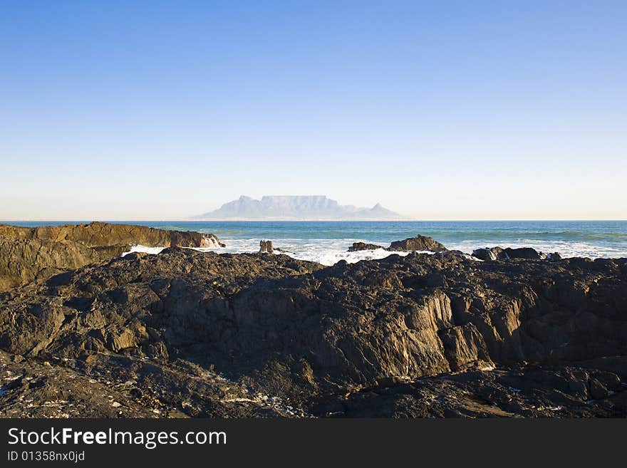 Table Mountain - the world famous landmark in Cape Town, South Africa. Picture taken on a clear Winters day from the Blouberg Strand beach. A rocky part of the beach is in the foreground. Table Mountain - the world famous landmark in Cape Town, South Africa. Picture taken on a clear Winters day from the Blouberg Strand beach. A rocky part of the beach is in the foreground.