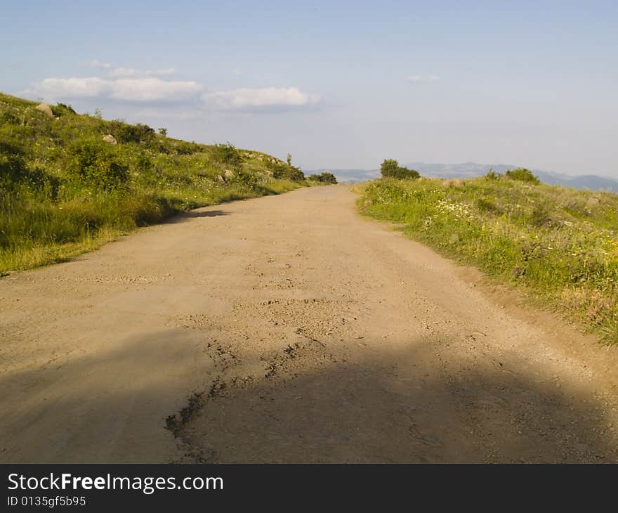 Dirty rural road, green meadow, blue sky. Dirty rural road, green meadow, blue sky.