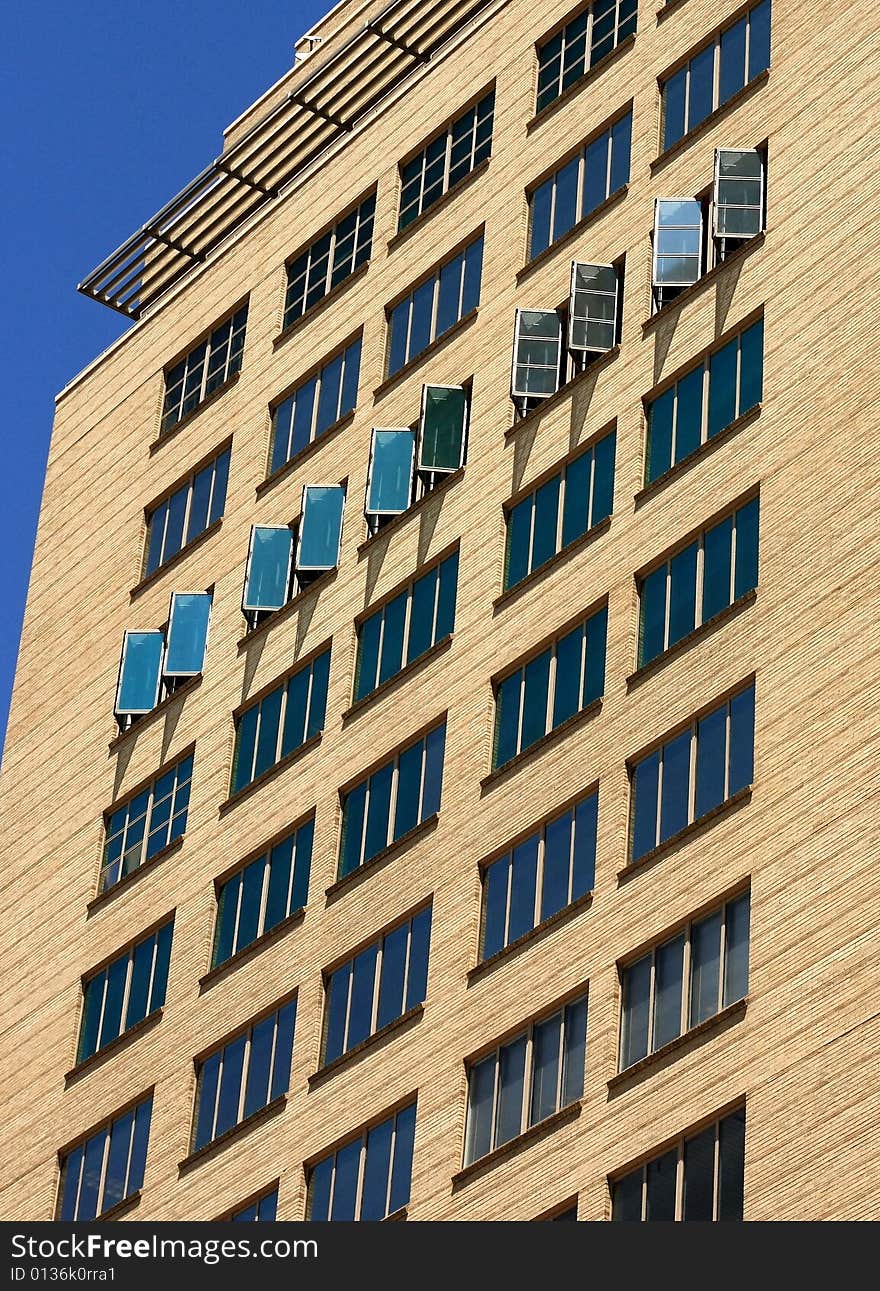 One row of open windows among rows of windows on modern tan brick city building on hot summer day