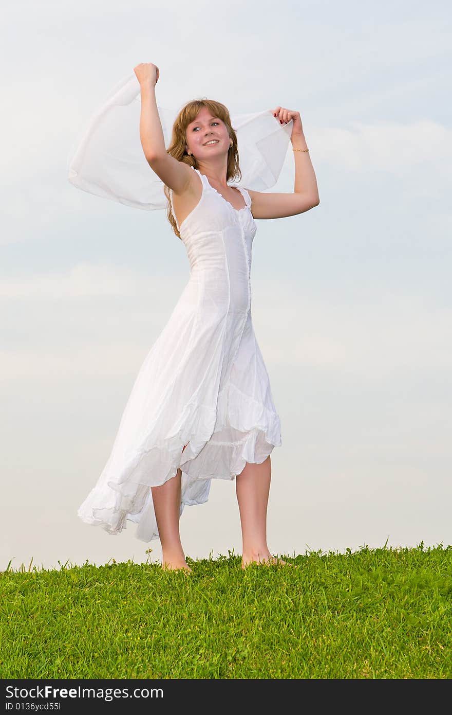 Girl with a white scarf in a hand stands on a green grass on a background of the blue sky. Girl with a white scarf in a hand stands on a green grass on a background of the blue sky