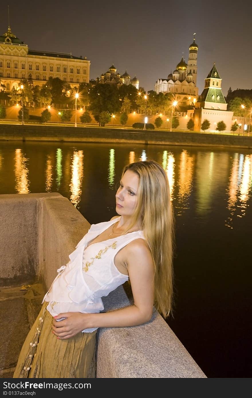 Beautiful blonde woman standing near a river in the city at night time. Beautiful blonde woman standing near a river in the city at night time