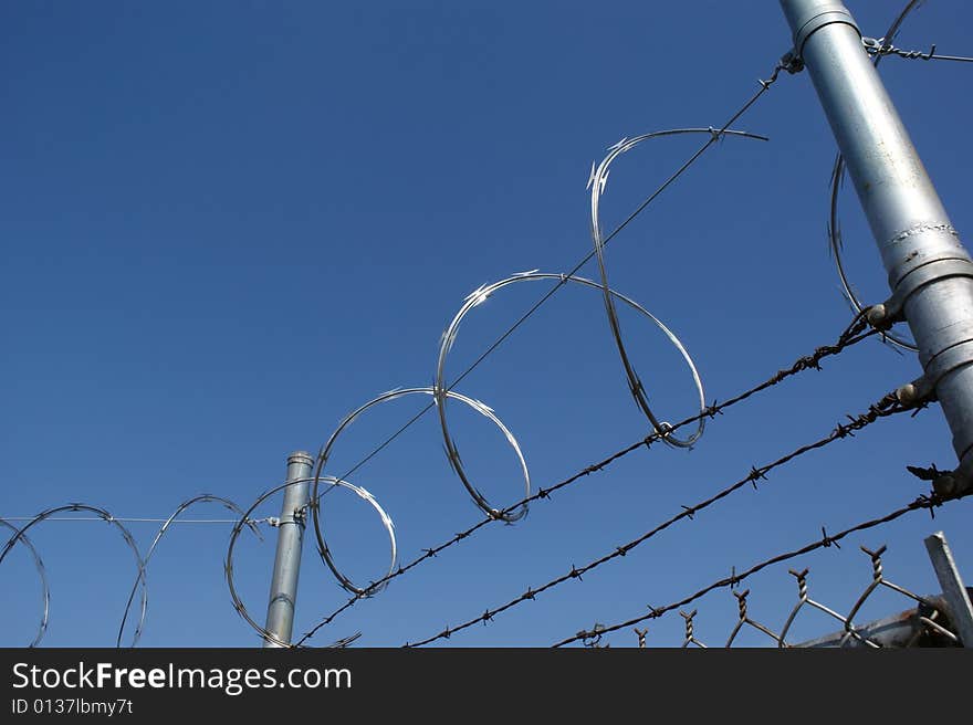View of razor wire and barbed wire atop a fence.