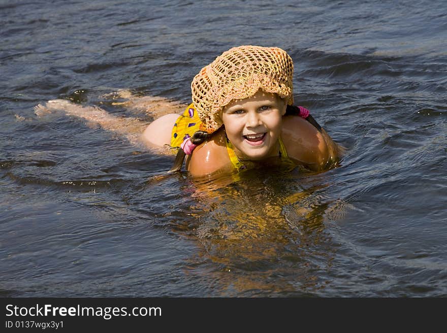 Little girl in orange hat swimming in a river in the summer. Little girl in orange hat swimming in a river in the summer