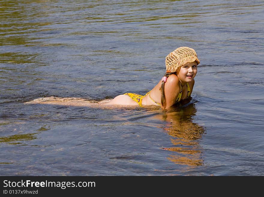 Little girl in orange hat swimming in a river in the summer. Little girl in orange hat swimming in a river in the summer