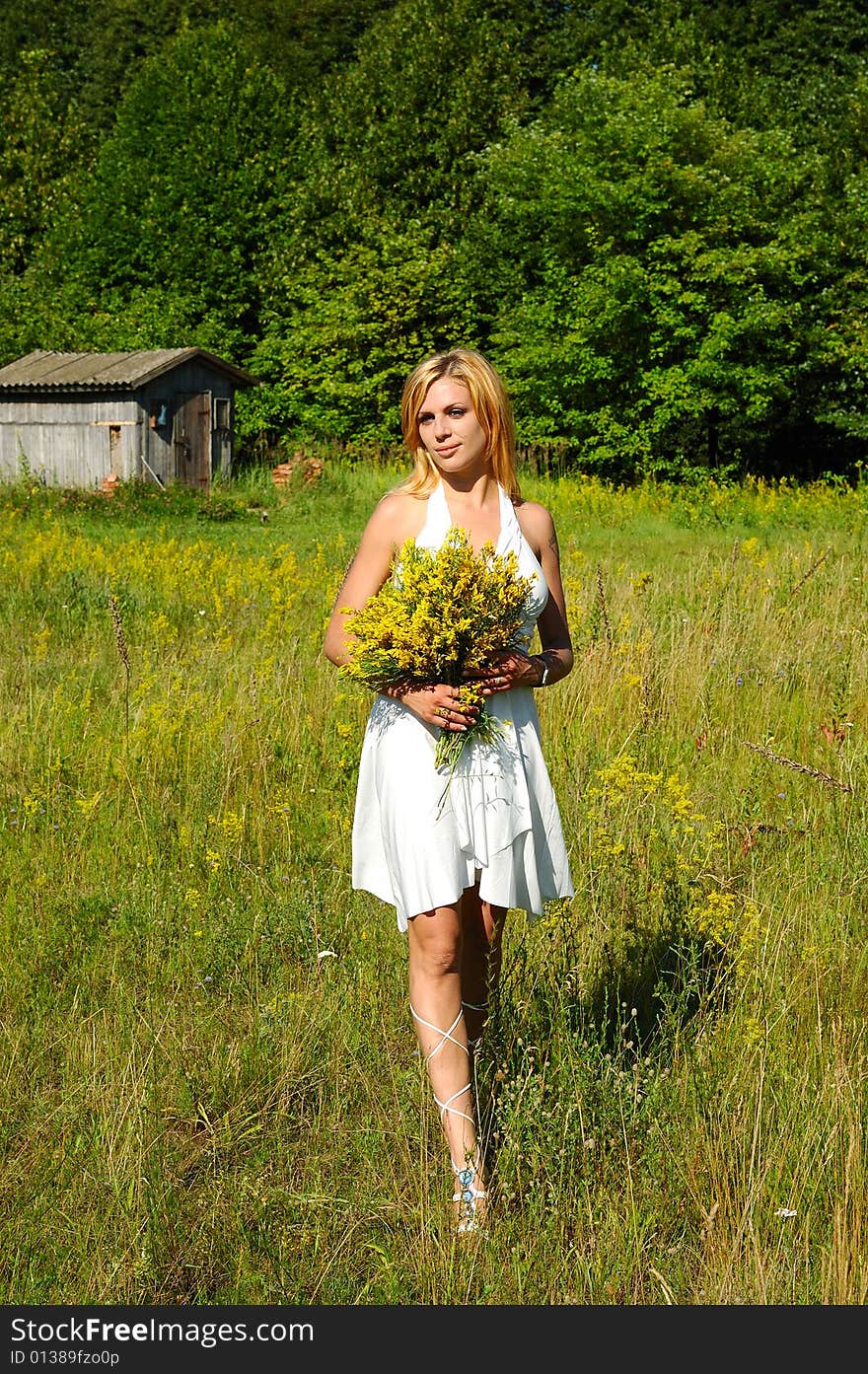 Blond woman in white dress walking through the meadow