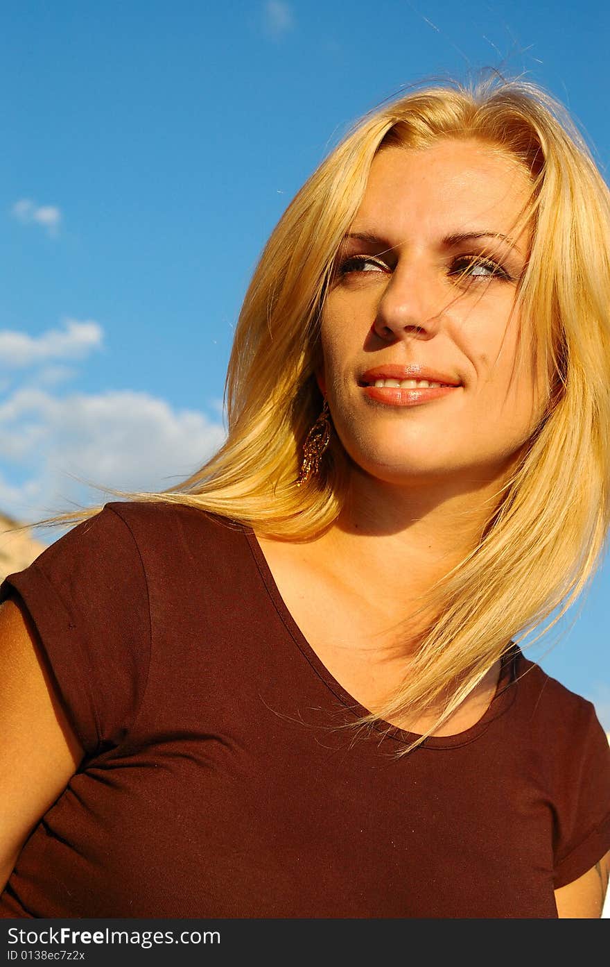 Smiling blond woman with fly-away hair against blue sky. Smiling blond woman with fly-away hair against blue sky