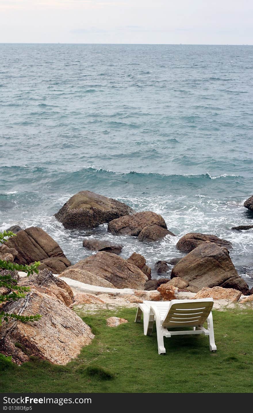 White deck chair overlooking the ocean with rocks on the shore.
