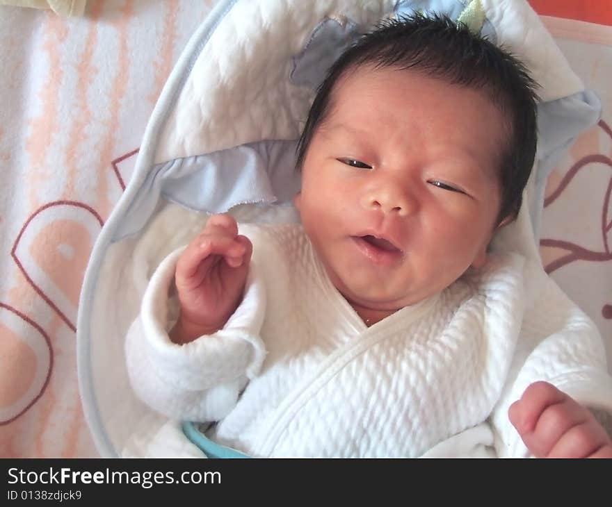 A Chinese baby is waving her hand on a bed. A Chinese baby is waving her hand on a bed