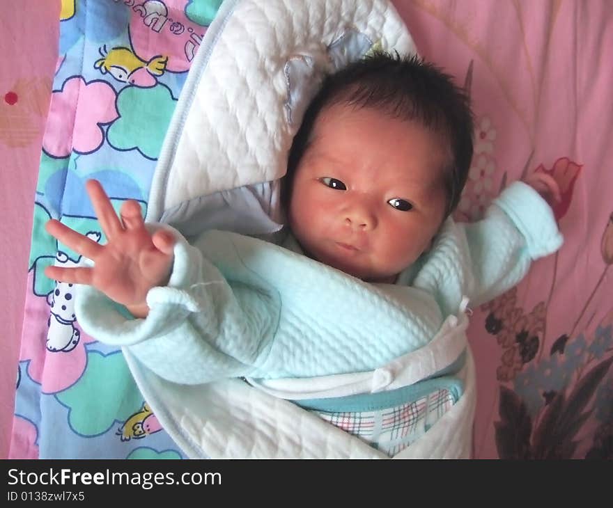 Lovely Baby in blue on a bed, making the gesture of 'OK'