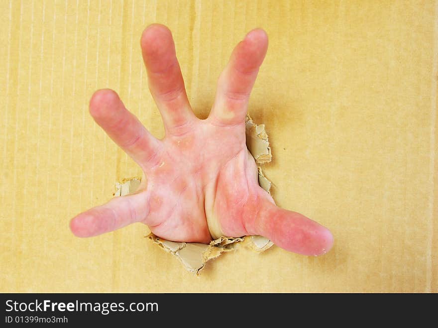 Hand opening a hole in brown cardboard