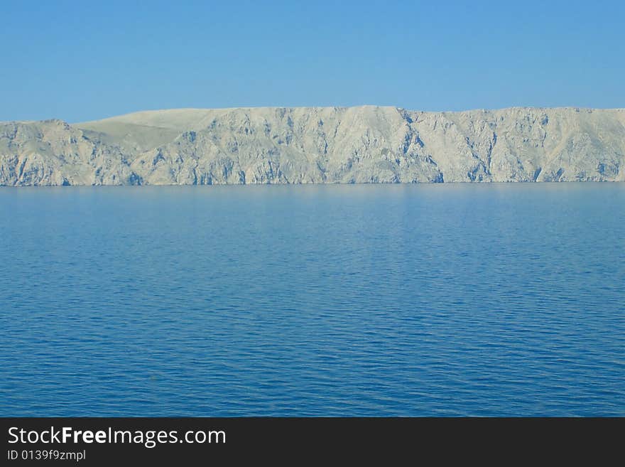 Beautiful panoramic view of the bear coastline of island against blue rippled sea and clear blue morning sky Postcard: island Krk, Croatia *with space for text (copyspace). Beautiful panoramic view of the bear coastline of island against blue rippled sea and clear blue morning sky Postcard: island Krk, Croatia *with space for text (copyspace)