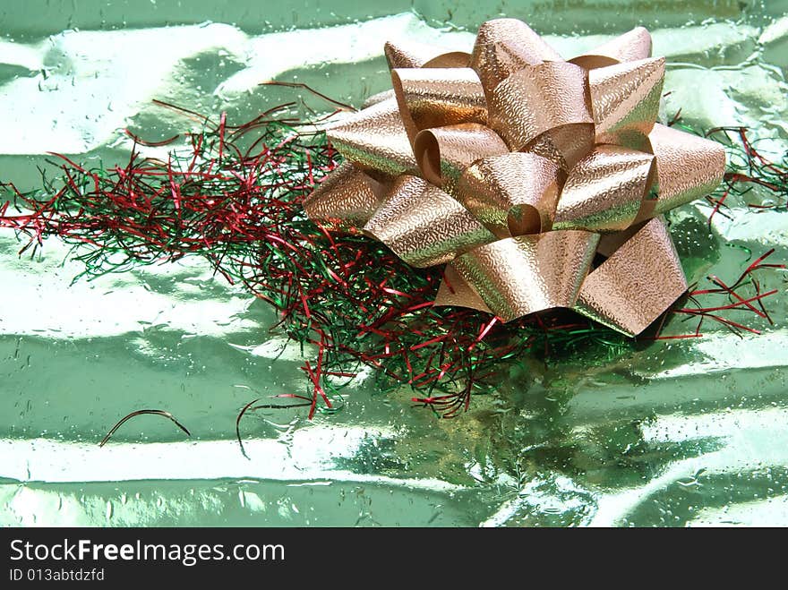 Gold foil bow on green foil wrapping paper with red and green tinsel. Gold foil bow on green foil wrapping paper with red and green tinsel