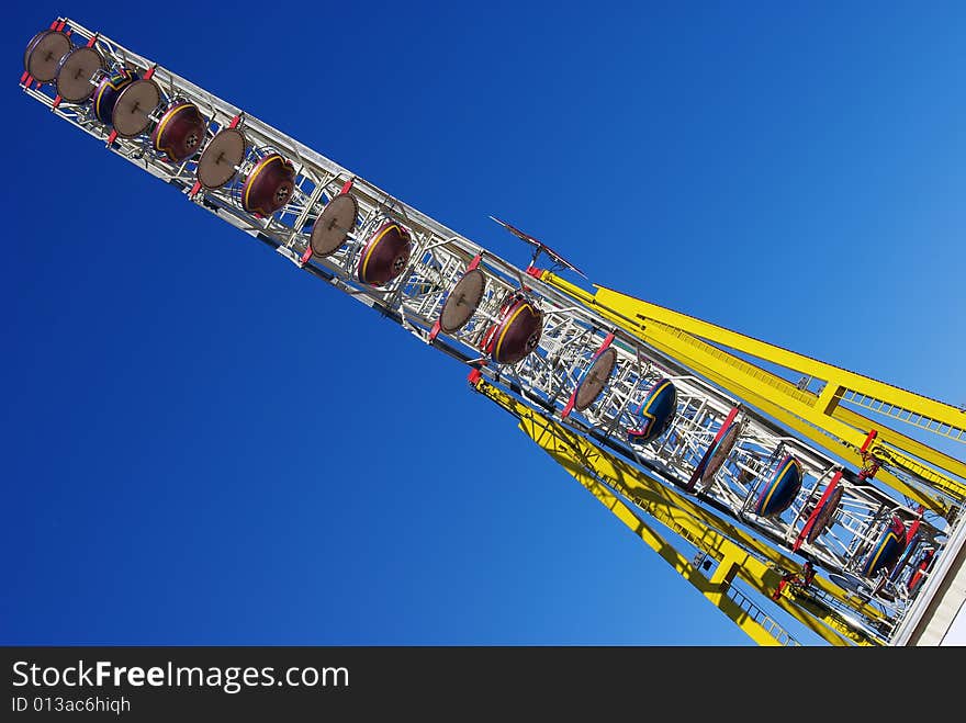 Funfair ferris wheel in profile. Empty wheel boxes resting over blue summer sky. Funfair ferris wheel in profile. Empty wheel boxes resting over blue summer sky.