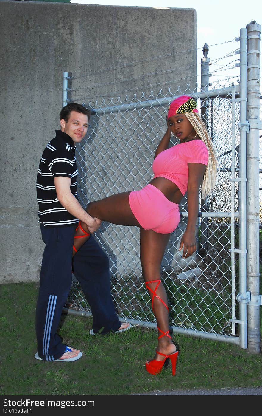 An pretty Jamaican model on location in front of a wire fence with a young man holding her leg. An pretty Jamaican model on location in front of a wire fence with a young man holding her leg.