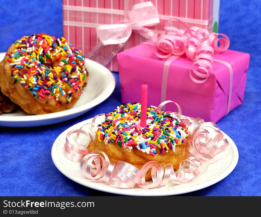 Pretty party donuts festively decorated with sprinkles, a candle and ribbons in front of beautiful pink gift boxes. Pretty party donuts festively decorated with sprinkles, a candle and ribbons in front of beautiful pink gift boxes.