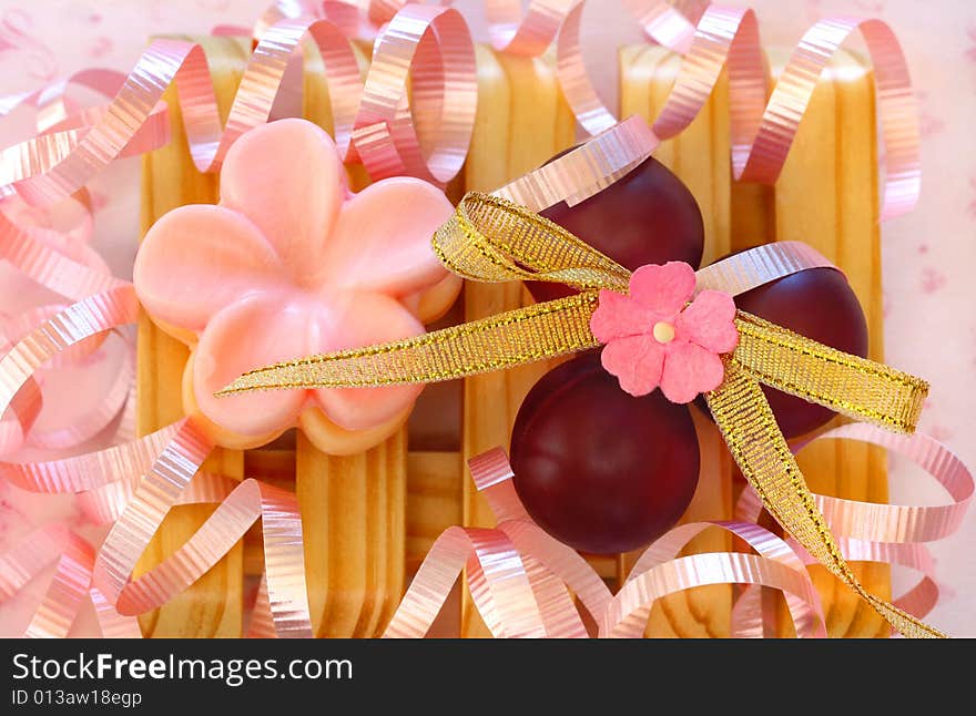 Pretty soap and bath beads on a wooden soap tray surrounded by pink ribbons. Pretty soap and bath beads on a wooden soap tray surrounded by pink ribbons.