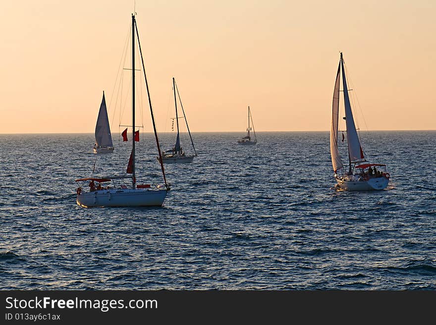 Five yachts sailing on sunset in calm sea