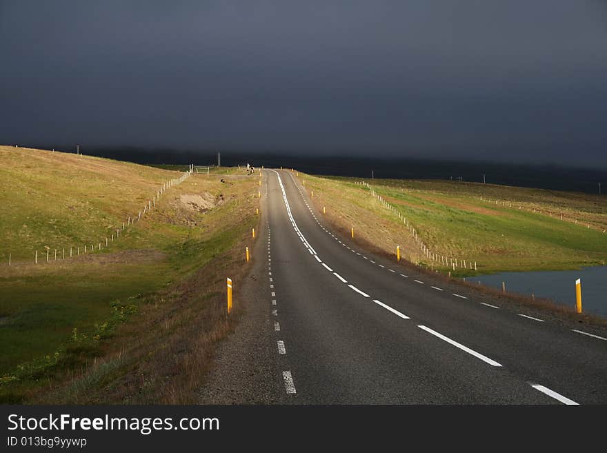 A road partially lit by sun with a dramatic background of stormy clouds. A road partially lit by sun with a dramatic background of stormy clouds.