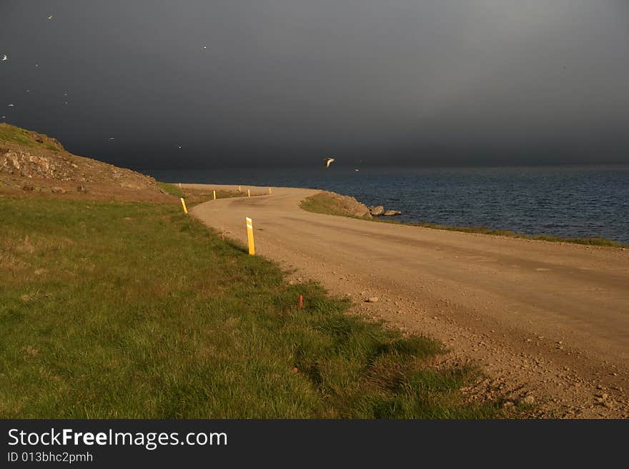 A road partially lit by the sun with a dramatic background of stormy clouds. A road partially lit by the sun with a dramatic background of stormy clouds.