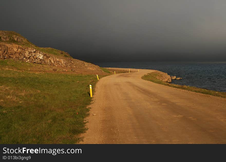 A road partially lit by the sun with a dramatic background of stormy clouds. A road partially lit by the sun with a dramatic background of stormy clouds.